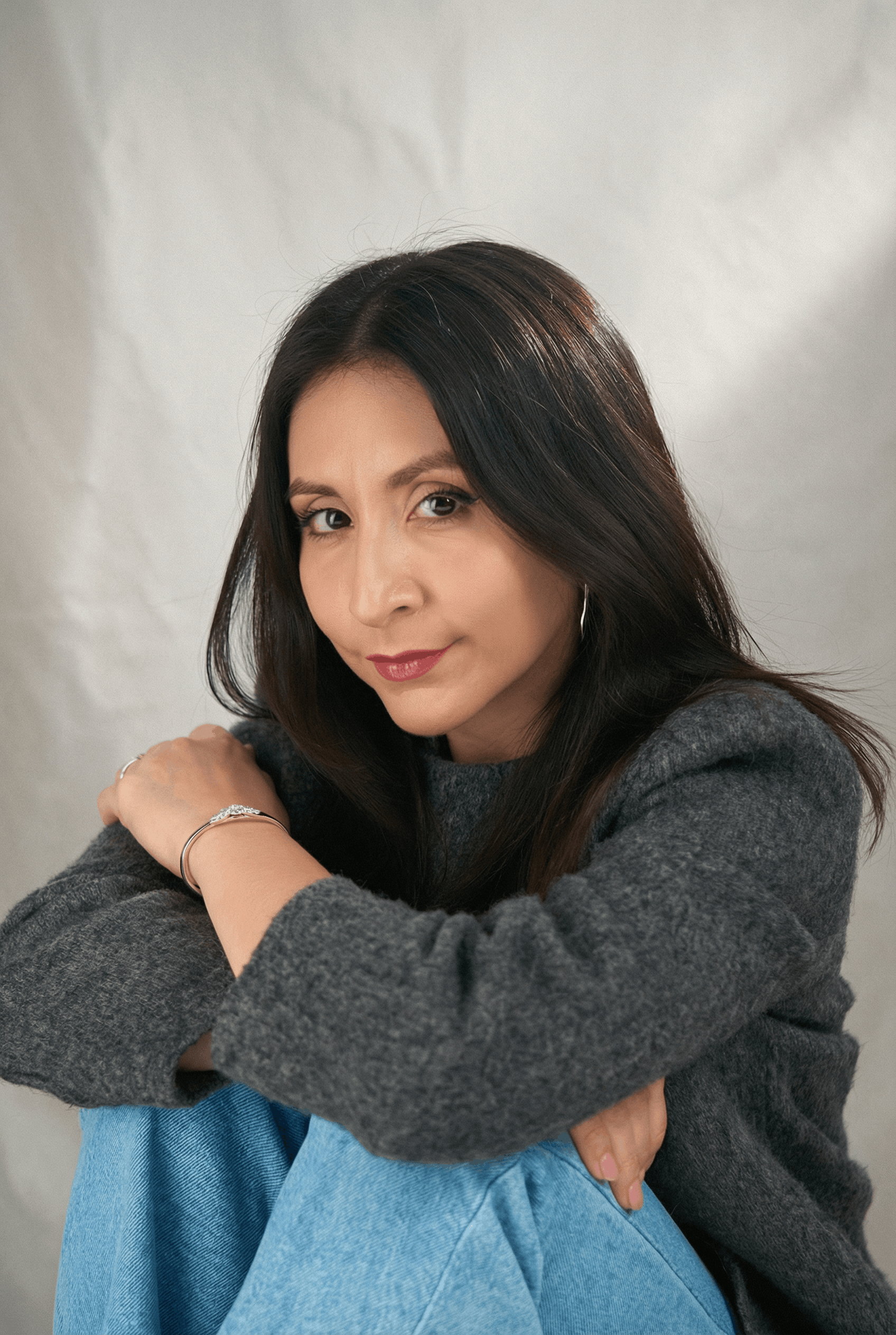 Retrato de Vane abrazando sus rodillas con sweater gris